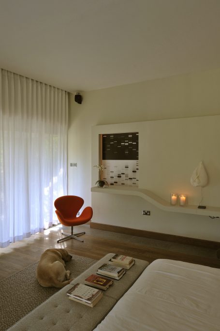 Chambre moderne avec fauteuil orange, lit, et un chien au sol. Ambiance lumineuse et minimaliste.
