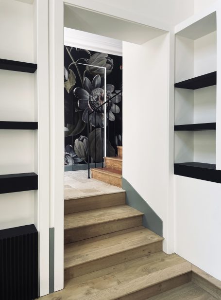 Intérieur moderne avec escaliers en bois et mur décoré de motifs floraux.